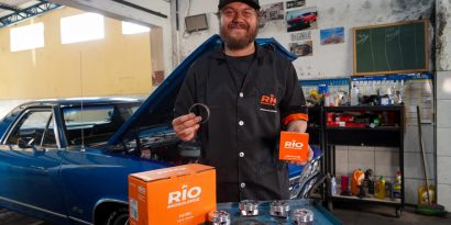 Um mecânico segurando anéis de pistão em uma mão, na outra uma embalagem de anéis de pistão. Em sua frente, uma mesa com uma caixa de pistão e alguns pistões em cima da mesa. Por que substituir aneis de pistão